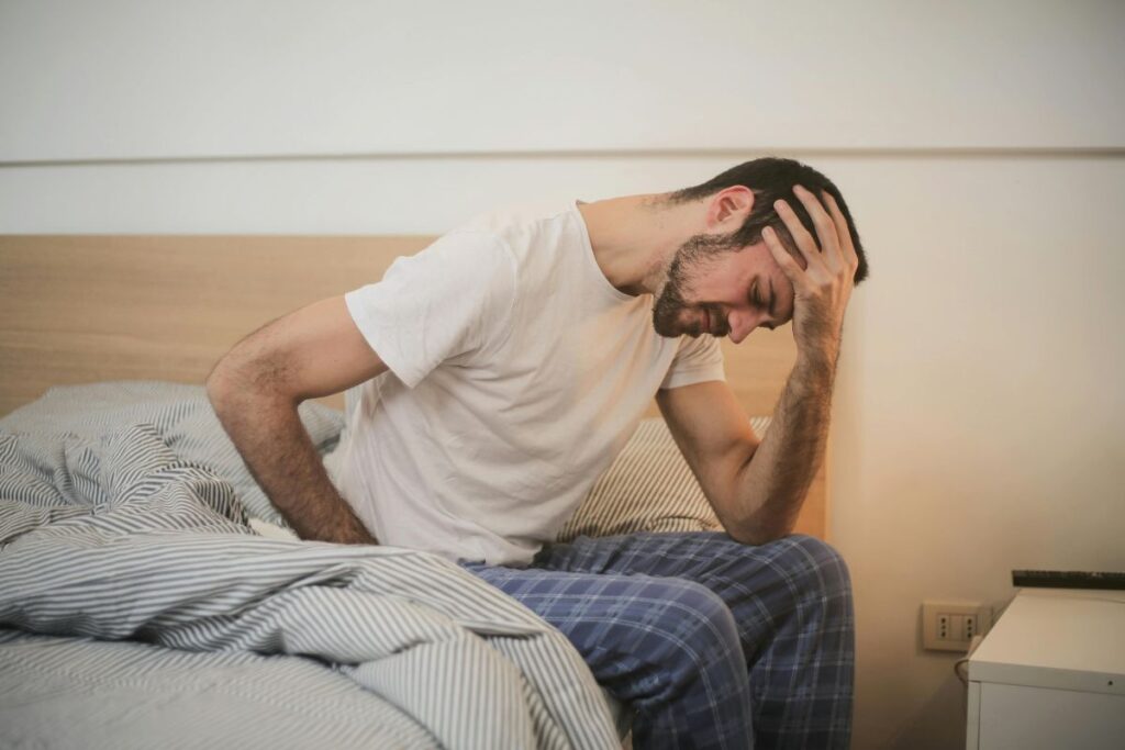Man sitting on bed holding his head in the morning due to headache after waking up