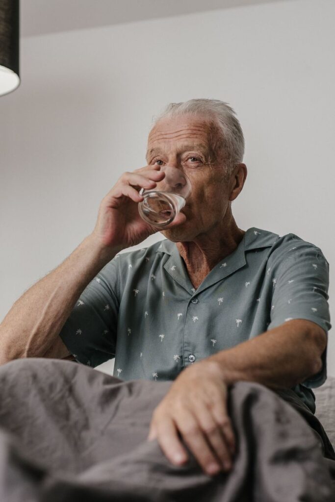 Person sitting on bed drinking water because of dehydration - waking up with a dry mouth