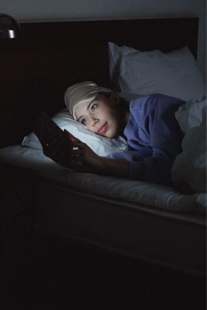 woman lying in bed looking at her phone can`t sleep because of noise (light sleeper)